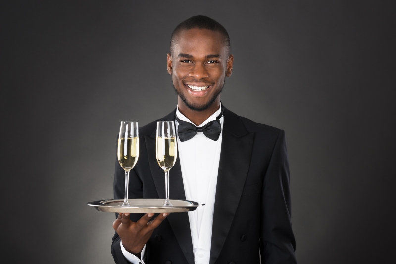 african waiter holding champagne drink against black background